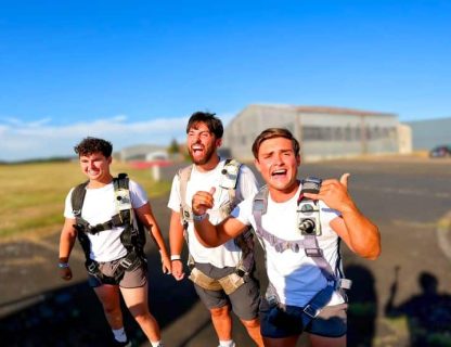 Groupe d'amis célébrant leur expérience de saut en parachute au sol devant un hangar