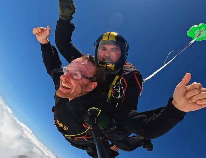 Sauteur souriant en chute libre avec son moniteur, extracteur vert déployé, nuages au-dessus de la Touraine