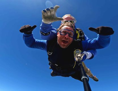 Sauteur pouces levés en chute libre, moniteur tandem derrière lui, ciel bleu sans nuage